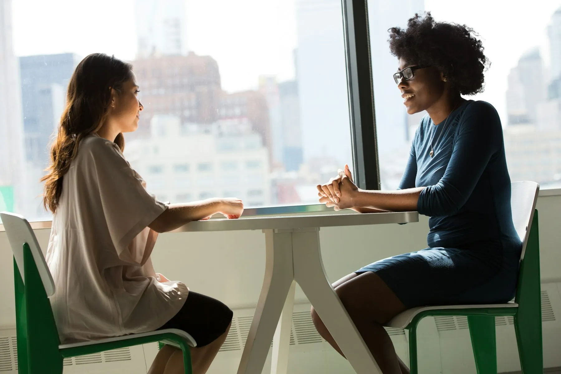 Twee vrouwen in gesprek aan een tafel bij het raam